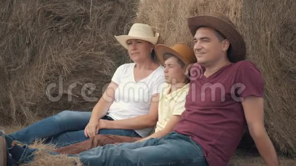 幸福的家庭母亲父亲和儿子拿着一块石板坐在地里靠在干草卷上快乐的概念视频的预览图