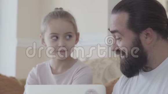 爸爸和可爱的女儿和笔记本电脑坐在沙发上的客厅里谈论一些有趣的事情的画像视频的预览图