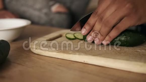 特写一个年轻迷人快乐的穆拉托人切黄瓜做沙拉的慢镜头他正在制作视频的预览图
