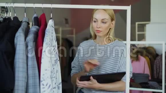 服装店老板正在检查和计数铁轨上的服装同时使用平板电脑她在输入视频的预览图