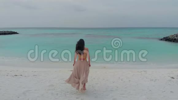穿着长裙走向海洋的年轻女子视频的预览图