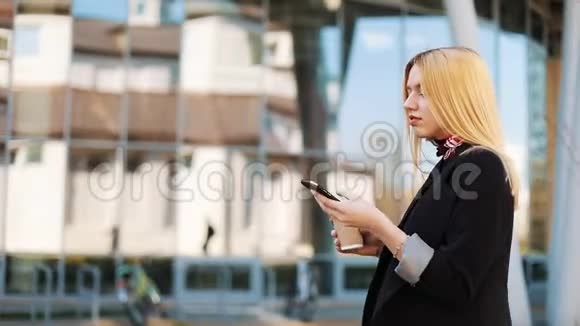 年轻的女士端着一杯咖啡沿着外面的镜子墙走在她的智能手机里输入一些东西视频的预览图