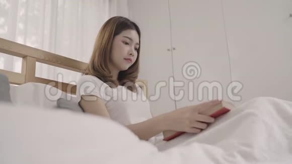 美丽迷人的年轻亚洲女人早上躺在床上放松时在家里的卧室里看书视频的预览图