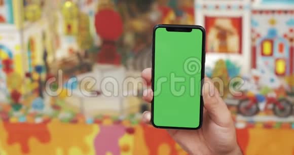 特写一个男人手拿着一部移动电话街道上有一个垂直的绿色屏幕儿童商店在视频的预览图