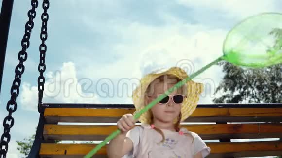 戴墨镜的小可爱女孩在蓝天上的跷跷板上摇摆视频的预览图