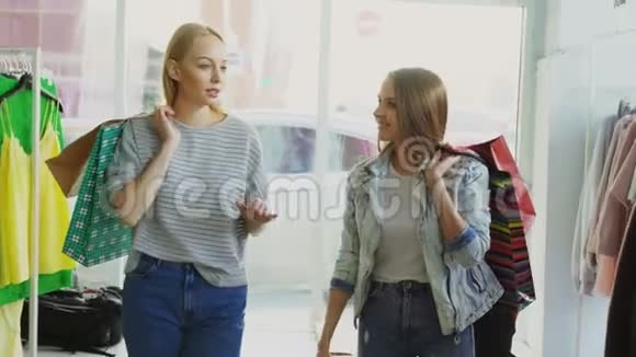 两个女孩用五颜六色的纸袋慢慢地走过宽敞的商店其中一个在说视频的预览图