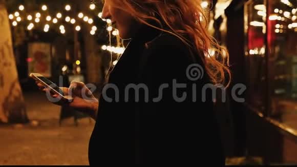浪漫的金发女人在等人晚上在智能手机上上网视频的预览图