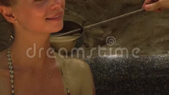 微笑的女人在水疗中心洗泥水美丽的女人在泥浆水疗中心洗澡从勺子里倒出身体健康视频的预览图