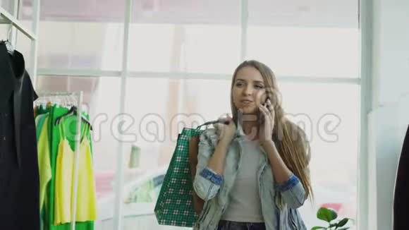 多莉拍摄了一个年轻女子穿过服装部门手里拿着袋子在手机上交谈很多很多视频的预览图