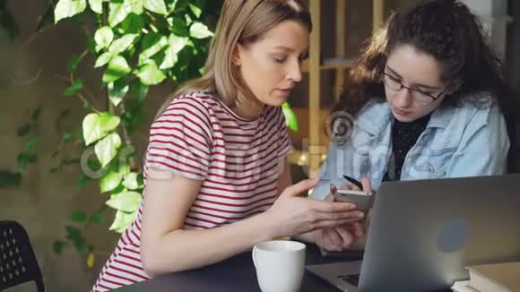 两名使用智能手机的女学生的特写漂亮的金发女孩摸着屏幕和她的朋友聊天视频的预览图