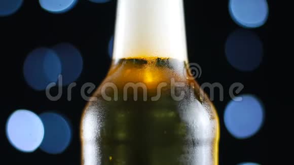 开着明亮的灯在黑色背景上旋转的透明瓶子里的冷啤酒视频的预览图
