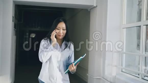 多莉拍摄的亚洲女学生走在宽阔的大学走廊上通过其他多民族的电话交谈视频的预览图