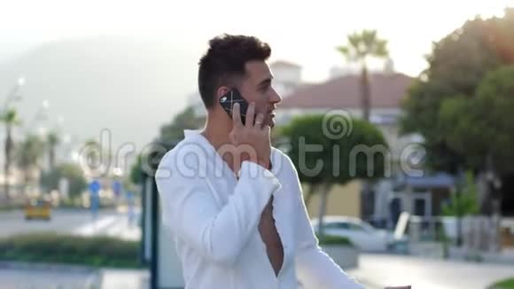 在度假时做远程工作微笑的男人沿着城市街道走打电话给智能手机视频的预览图