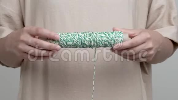 女人双手横着拿着一卷白绿色的绳子绳子垂下来比她把卷卷旋转到视频的预览图