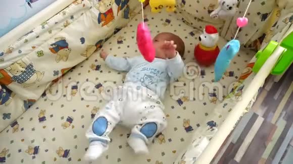 微笑宝宝躺在婴儿床上玩音乐旋转木马玩具视频的预览图