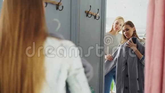 友好的女售货员正在帮助女顾客选择外套快乐的购物者站在前面的试衣间视频的预览图