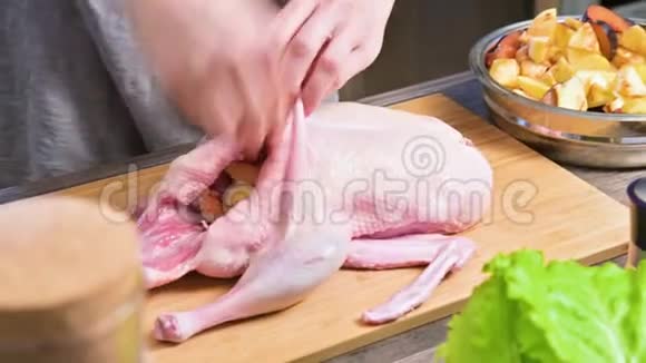 在家里的厨房里用特写的女性手准备烤鹅给鸭子装上苹果和水果原料食品视频的预览图