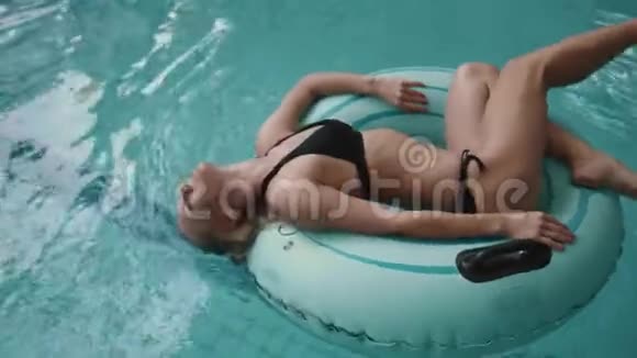 迷人的女士穿着黑色比基尼在游泳池里的充气橡胶圈上游泳时玩得很开心4k视频的预览图
