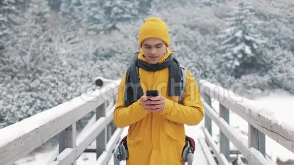 一位年轻的游客站在桥上使用智能手机冬天的时候美丽的山和白雪覆盖的湖视频的预览图