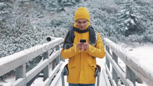 一位年轻的游客站在桥上使用智能手机冬天的时候美丽的山和白雪覆盖的湖视频的预览图