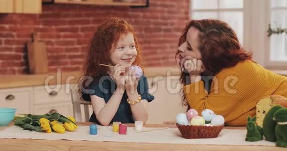 妈妈和她的小女儿正在准备复活节小女孩在舒适的厨房里画复活节彩蛋微笑的母亲视频的预览图