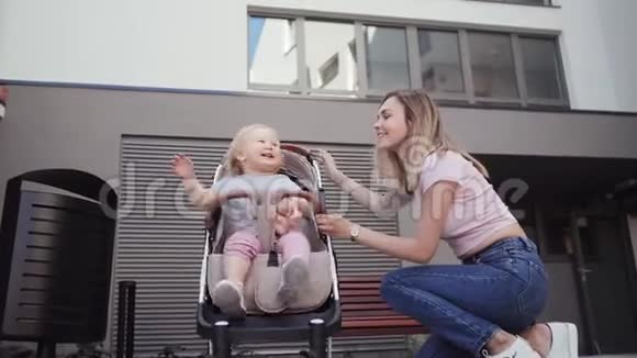 年轻的母亲和一个小女孩一起走女儿坐在房子附近的婴儿马车里视频的预览图