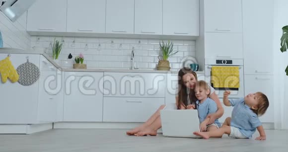 现代技术现代公寓爱妈妈和两个小儿子坐在客厅的地板上看着视频的预览图