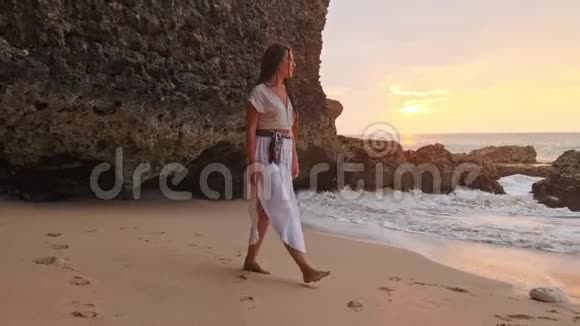 幸福的女人站在沙滩上向天空举手目标模糊了在洞穴旁边表达喜悦的女人视频的预览图