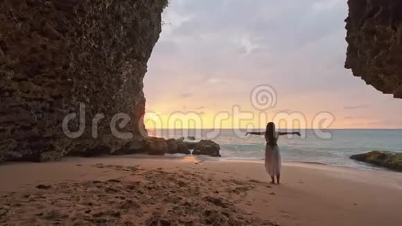 幸福的女人站在沙滩上向天空举手主题是模糊的在洞穴旁边表达喜悦的女人视频的预览图