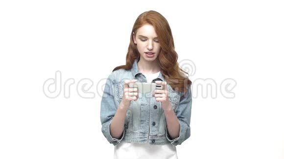 年轻快乐的女人在白色工作室的智能手机上玩游戏超级慢动作视频的预览图