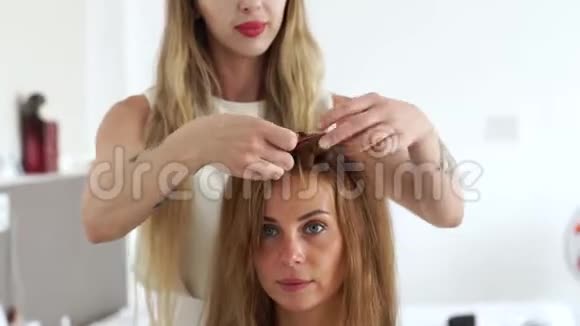 面对年轻女性同时在美容工作室创造发型理发师给长棕色的女人做时尚发型视频的预览图