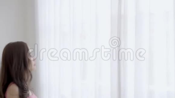 早上美丽的年轻亚洲女人醒来打开窗帘走向窗户视频的预览图