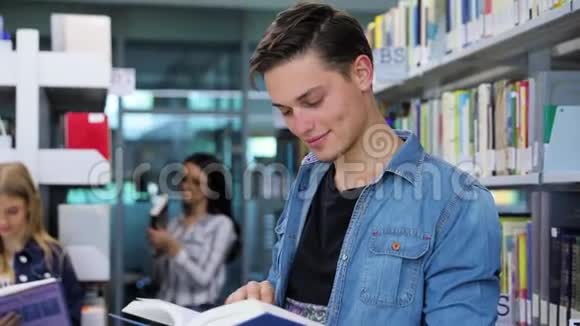 图书馆微笑男学生阅读书附近的书架视频的预览图