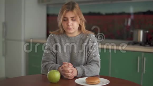 肖像年轻胖乎乎的女孩认为她应该吃美味的汉堡包或多汁的绿色苹果困难的选择视频的预览图