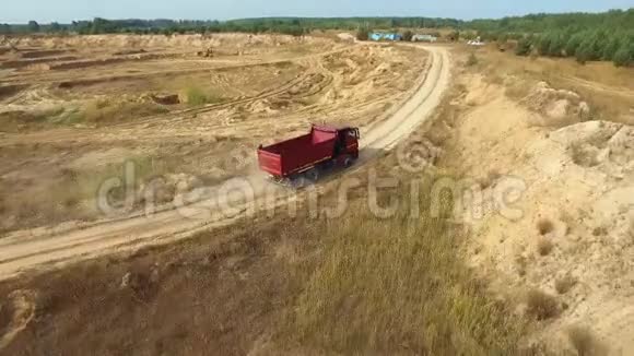 夏季红色自卸卡车在靠近森林的采石场的沙路上行驶的鸟瞰图场景工业视频的预览图