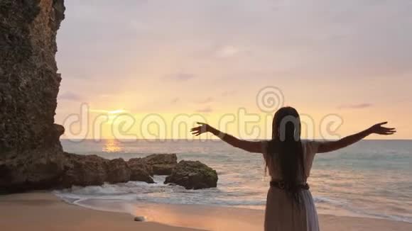幸福的女人站在沙滩上向天空举手目标模糊了在洞穴旁边表达喜悦的女人视频的预览图