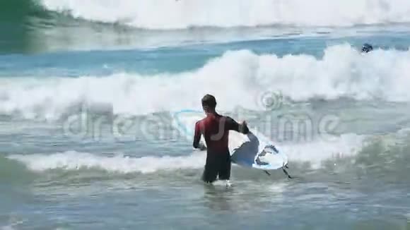 穿着冲浪服装进入海洋的人手里拿着冲浪板积极运动视频的预览图
