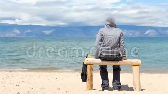 男人或女人坐在海滩上的帽衫里后景时间间隔4K视频的预览图