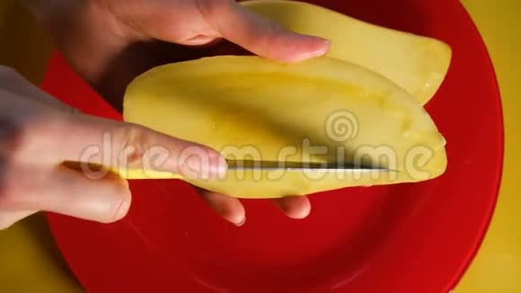 女孩切一个成熟的泰国芒果刀切在红色盘子和黄色背景的切片上俯视视频的预览图