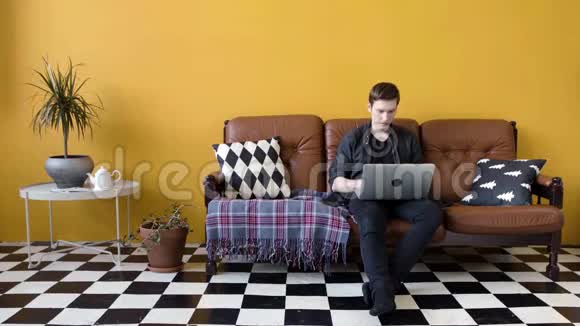 年轻人坐在沙发上用笔记本电脑工作库存录像年轻人在笔记本电脑上自由工作视频的预览图