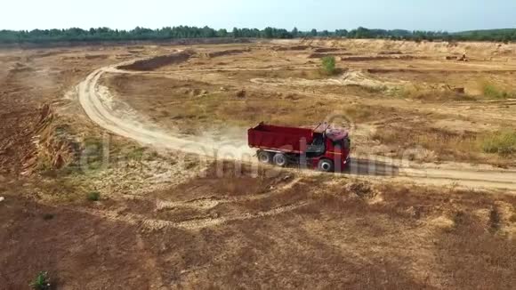 夏季红色自卸卡车在靠近森林的采石场的沙路上行驶的鸟瞰图场景工业视频的预览图