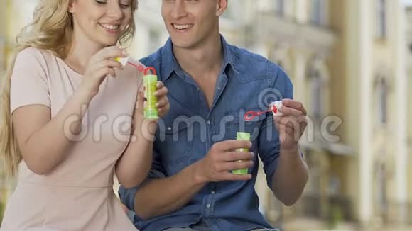 浪漫的情侣坐在长凳上吹着肥皂泡无忧无虑的生活视频的预览图