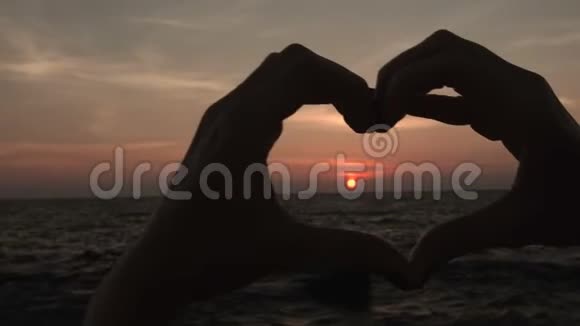 女人在夕阳下用手做心形标志女孩举起爱的象征视频的预览图