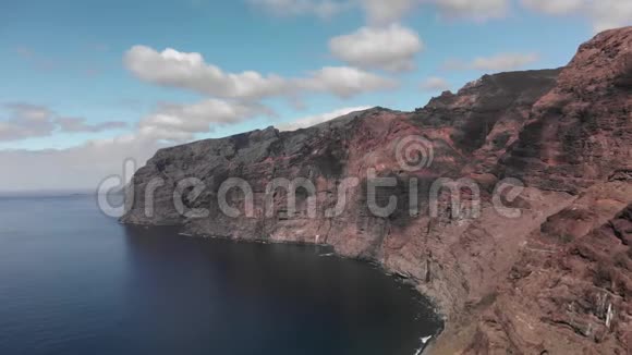 空中射击巨大的黑红色火山岩的海岸是海洋蓝色水域中的一座山与蓝色对抗视频的预览图