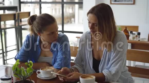 在咖啡馆里约会的女人分享她手机上令人兴奋的东西视频的预览图