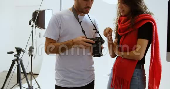 男子摄影师向女子模特展示数码相机4k的照片视频的预览图