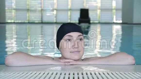 戴着帽子的年轻女人看着相机在游泳池里微笑视频的预览图