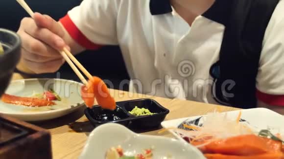 快乐的亚洲男孩吃日本食物的慢动作一个十几岁的孩子坐在咖啡馆里用棍子吃寿司视频的预览图