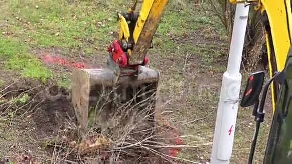 一台黄色的小挖掘机在建筑物附近工作一台的挖掘机装载土壤和根视频的预览图