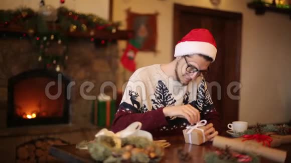 戴着圣诞帽的快乐男人在壁炉旁打开圣诞礼物盒里面有闪烁的花环微笑的家伙收到了视频的预览图